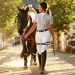 Lady in white jods leading horse down a lane