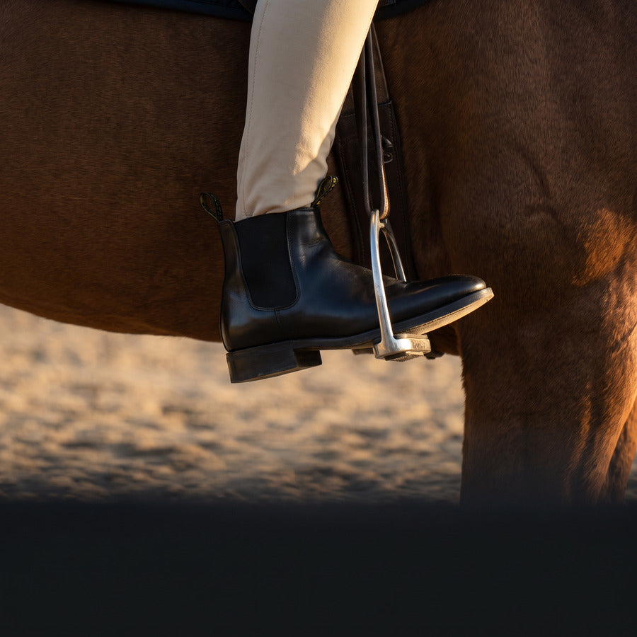 Rider's tall boot in a stirrup alongside a horse
