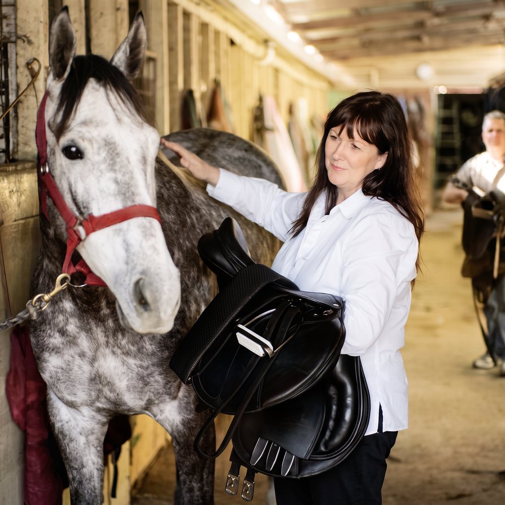 Bronwyn from Ascot Saddlery with a dressage saddle beside a grey horse